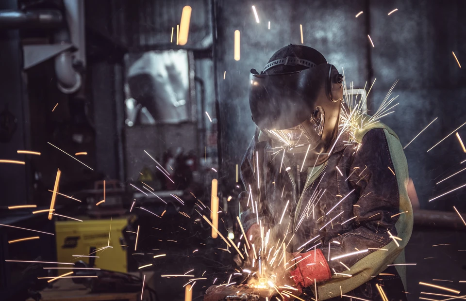 Atelier industriel intérieur avec soudeur en action portant masque de protection et vêtements de sécurité