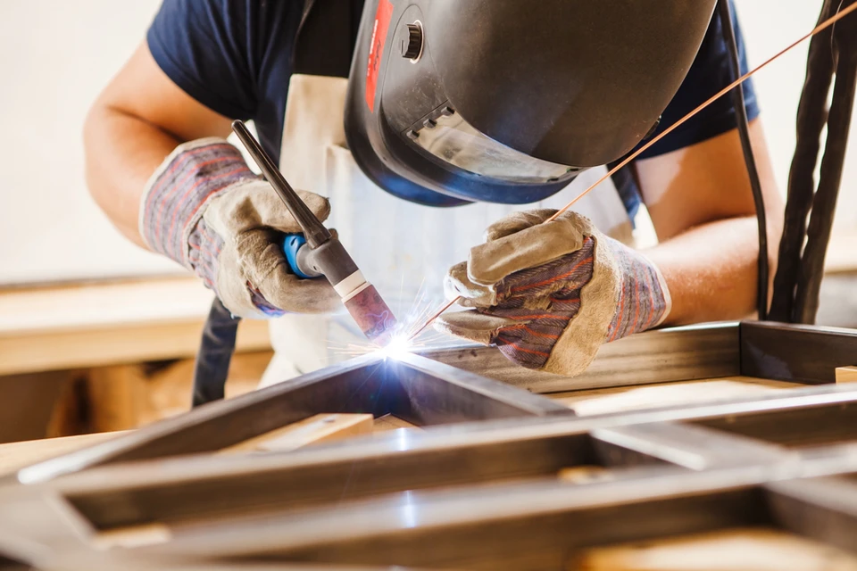 Atelier intérieur avec soudeur professionnel effectuant une soudure à l'arc sur structure métallique