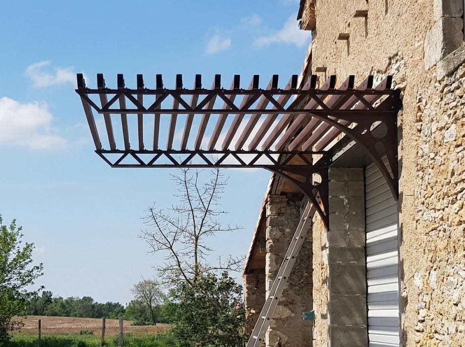 Pergola métallique en acier peint brun-rouge, fixée en encorbellement sur façade en pierre de taille