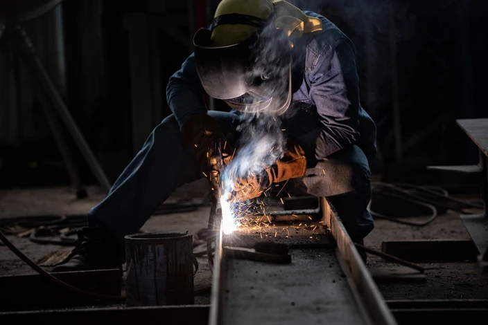 Un soudeur professionnel travaille dans un atelier industriel, portant un masque de protection et des gants