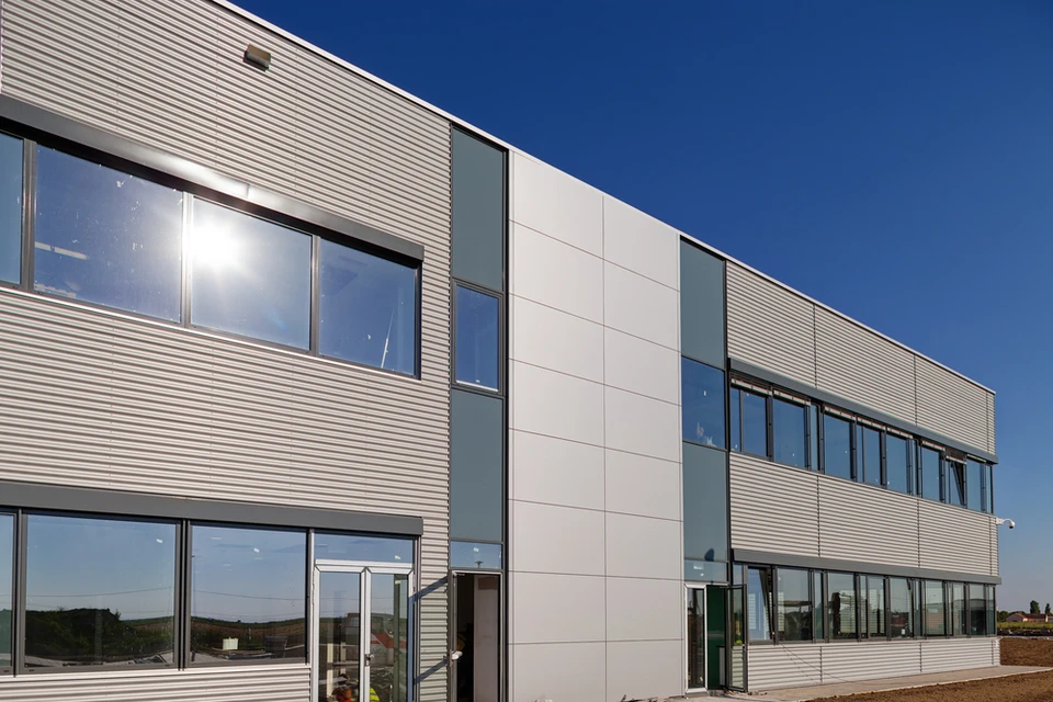 Façade extérieure de bâtiment avec bardage métallique blanc à lames horizontales sous ciel bleu