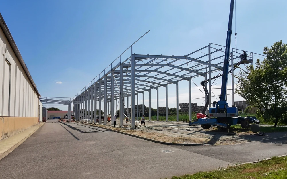 Structure métallique de charpente industrielle vue en contre-plongée, sans couverture, composée de fermes en acier avec membrures supérieures et inférieures, montants et diagonales en profilés plats boulonnés