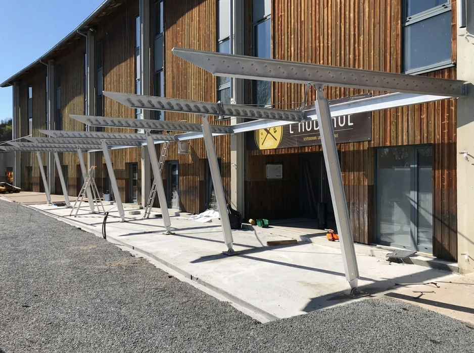 Structure métallique galvanisée en cours d'installation devant un bâtiment commercial à bardage bois vertical